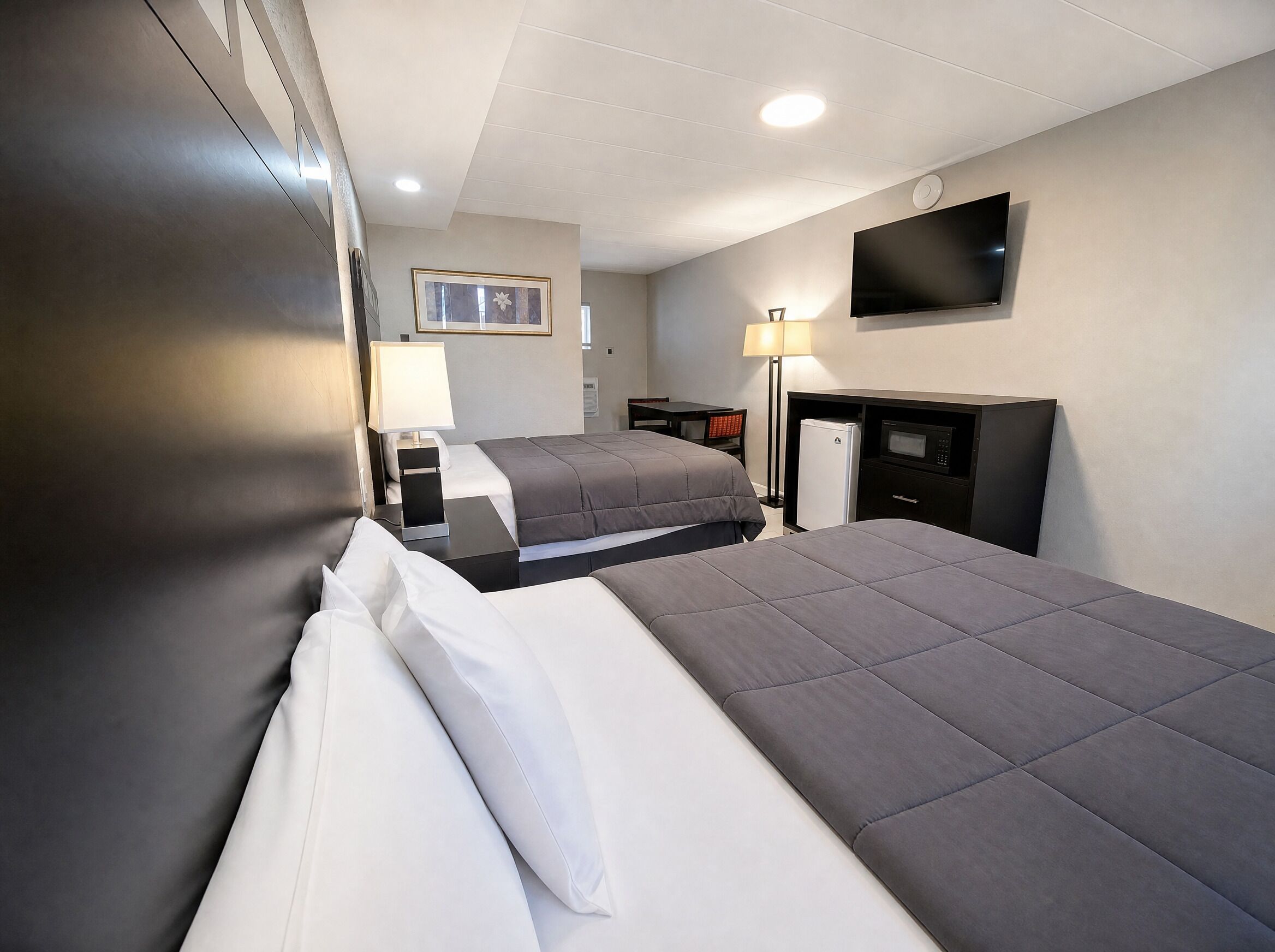 Une chambre d’hôtel avec deux lits, une télévision, un réfrigérateur, un bureau et une lampe.
