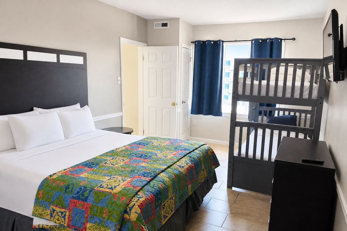 A bedroom with a bed, a bunk bed, a bedside table, and a window with curtains.