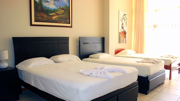 Habitación de hotel con dos camas, una mesita de noche con lámpara y obras de arte en las paredes.