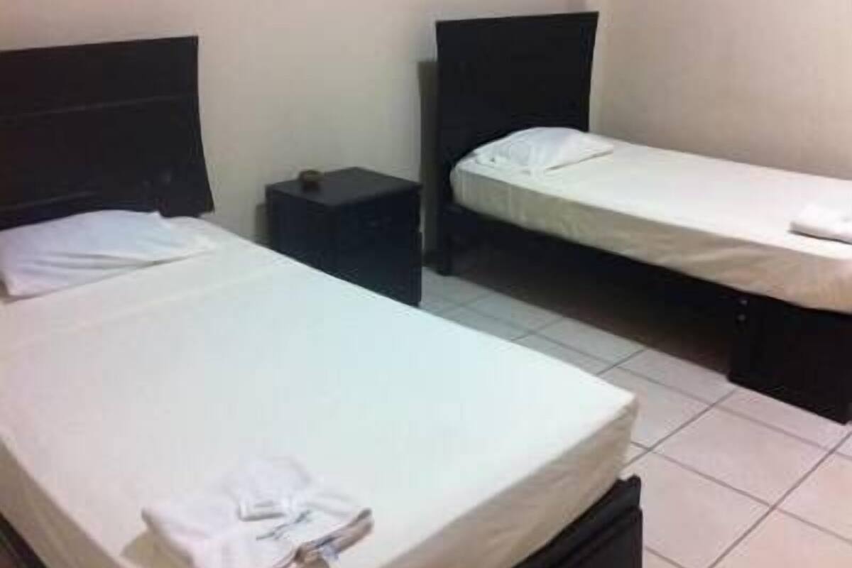 A small, simple room with two single beds, a nightstand, and a wall-mounted shelf.