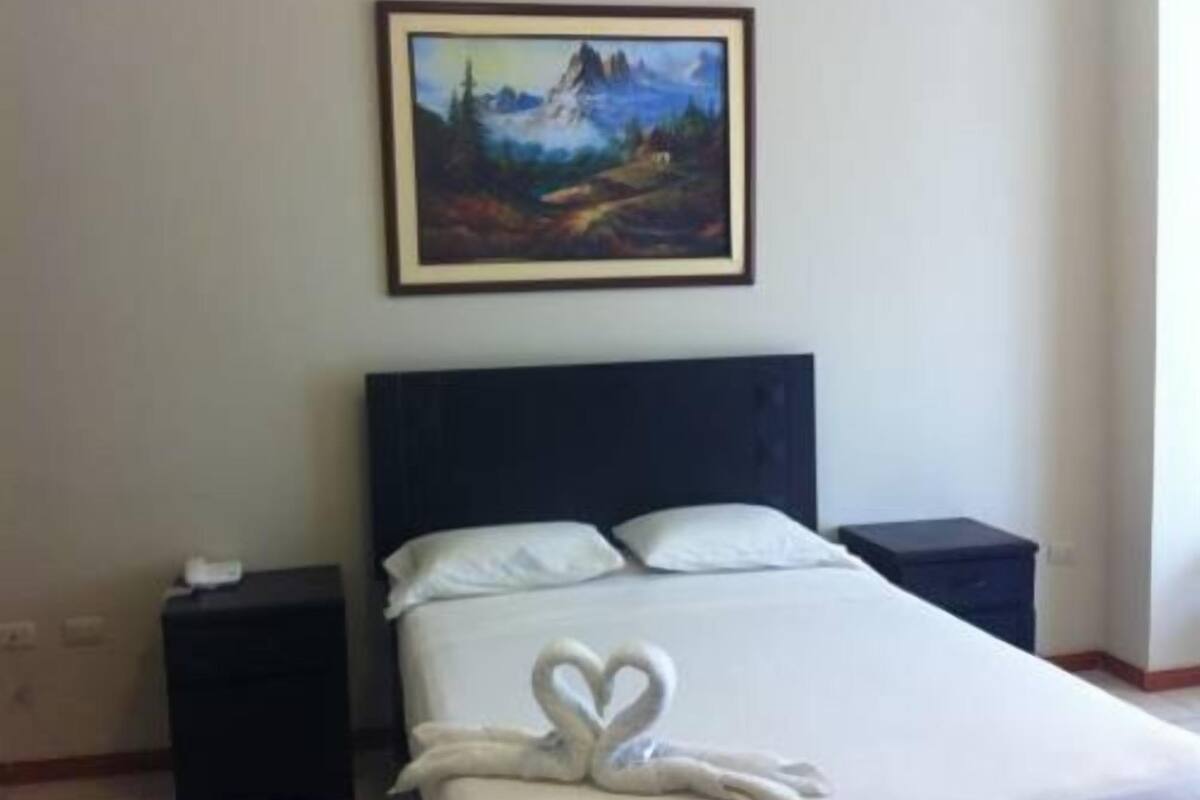 A hotel room with a bed, a painting on the wall, and a swan-shaped towel on the bed.