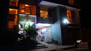 Un hotel moderno con una entrada bien iluminada, un área de recepción visible y una motocicleta estacionada afuera.