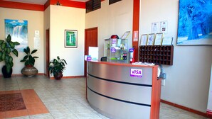 Un mostrador de recepción con un letrero de VISA, plantas en macetas, cuadros enmarcados y un extintor.