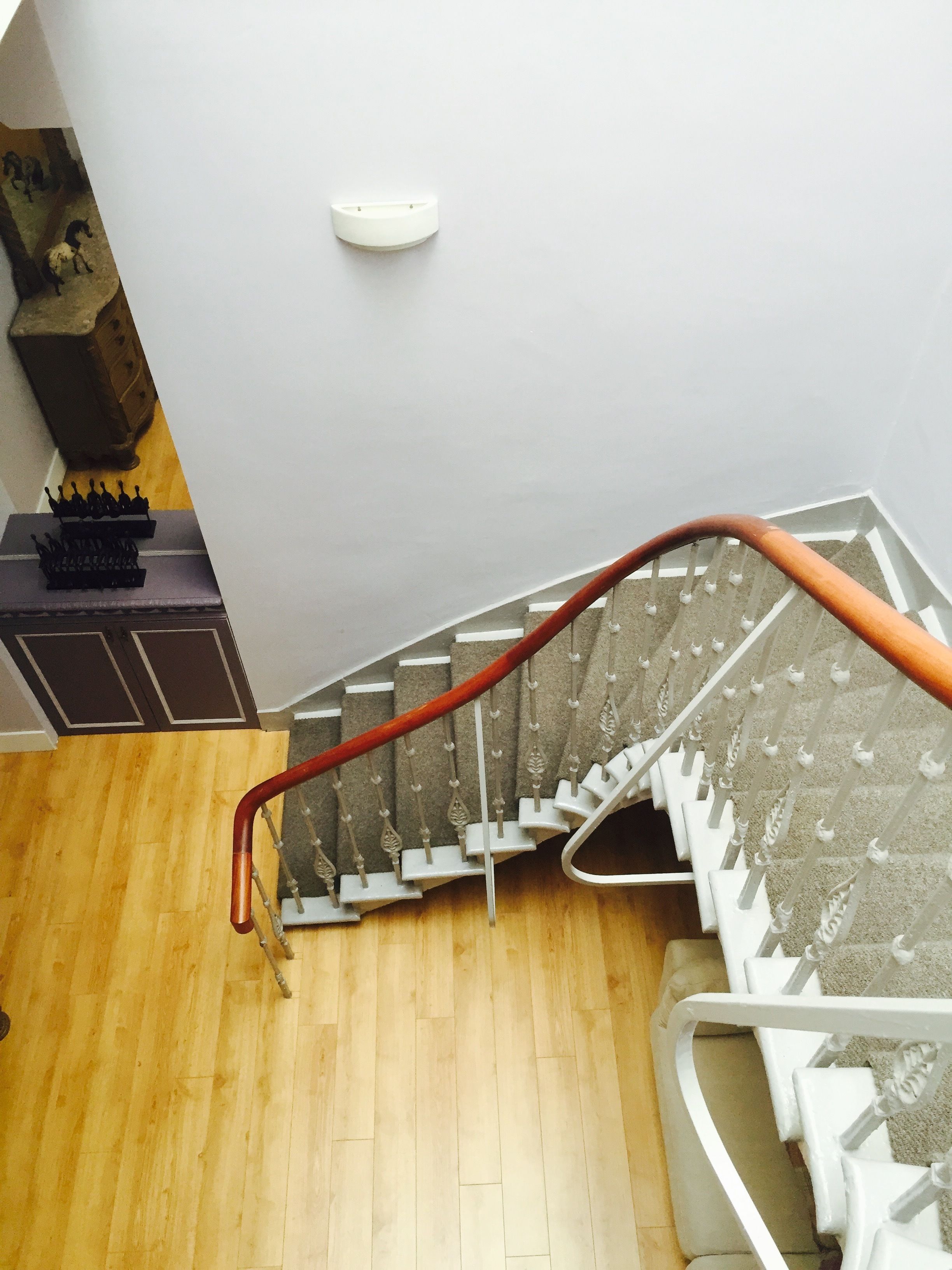 Un escalier en bois avec une rampe, un luminaire au-dessus et une commode de couleur sombre sur laquelle est posée une petite sculpture.