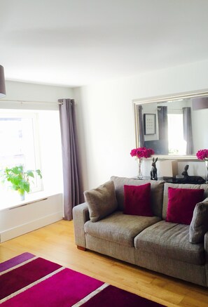 Una sala de estar con un sofá, un espejo y una ventana con cortinas.