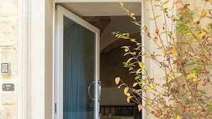 A doorway leading to a room with a tiled floor, a doormat, and a wall-mounted light switch.