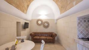 A cozy interior with a stone arch ceiling, a brown leather sofa, a round table with chairs, and a tiled backsplash.