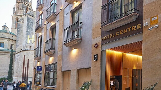 Entrada de un hotel con un letrero, una escalera y una vista de una torre histórica al fondo.