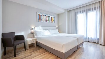 Una habitación de hotel con una cama, mesitas de noche, una silla y un cuadro en la pared.