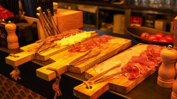 A wooden cutting board with various meats and cheese, a bowl of tomatoes, and wooden pepper mills.