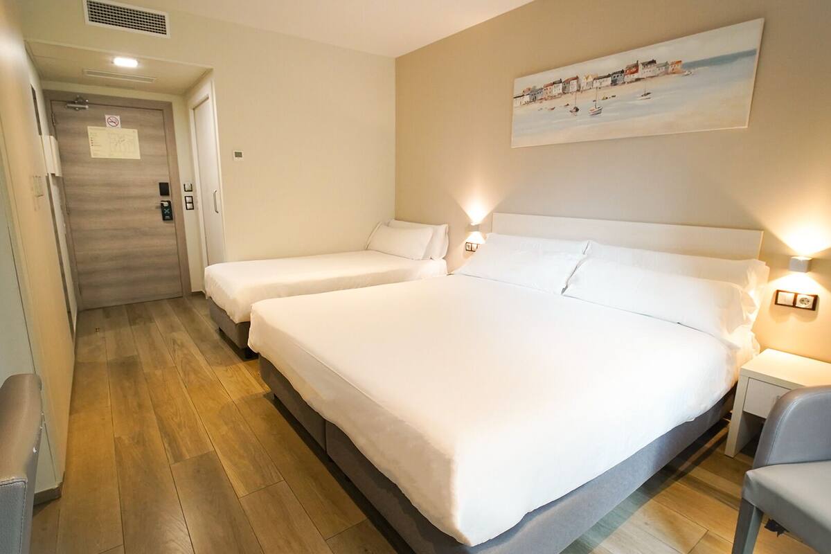 A hotel room with two beds, a painting on the wall, and a chair.