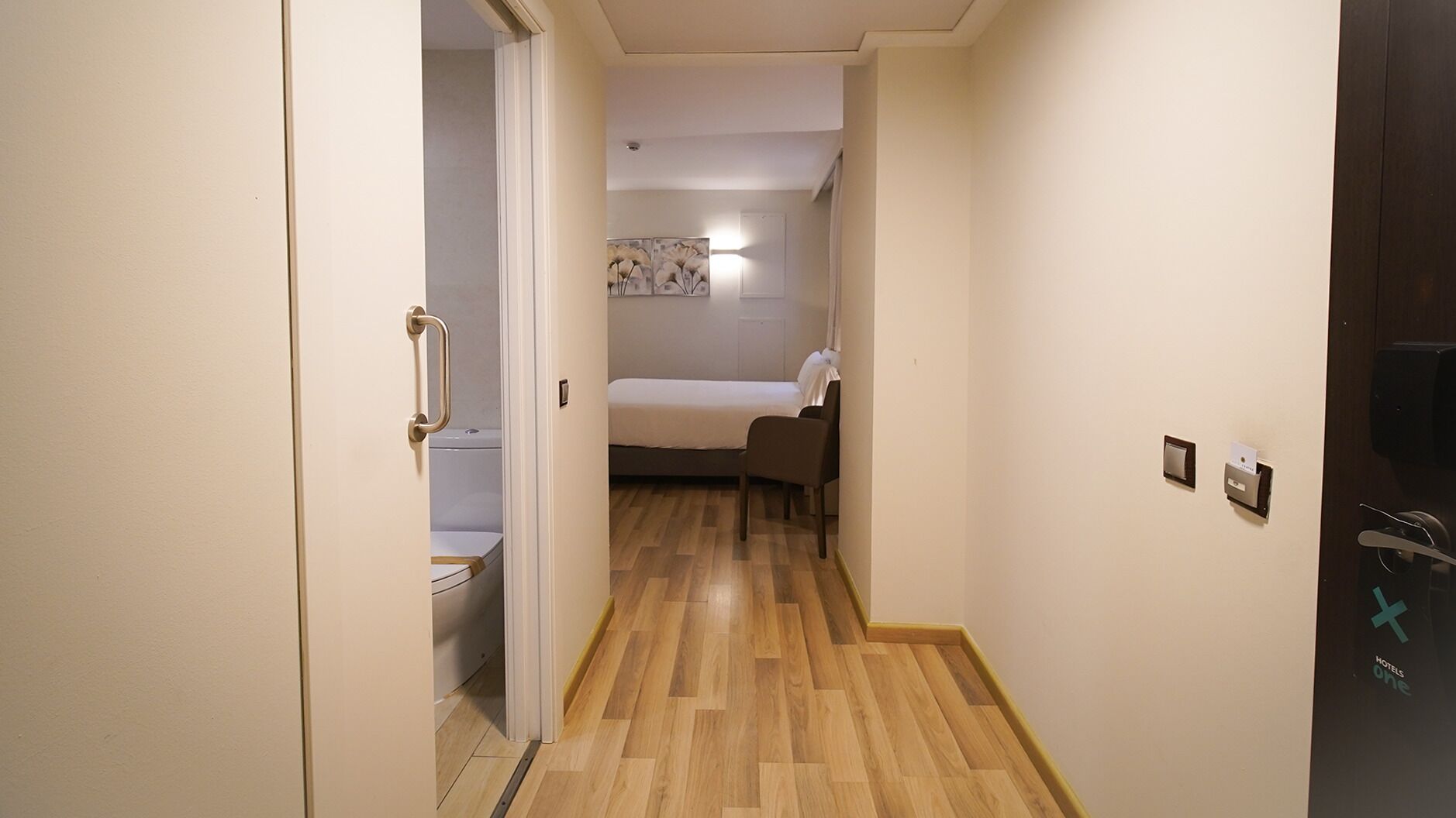 Un pasillo estrecho que conduce a un dormitorio con una cama, una silla y un inodoro.