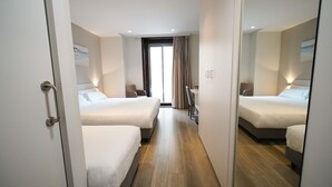Habitación de hotel con dos camas, un escritorio, una silla, un espejo y una ventana con cortinas.