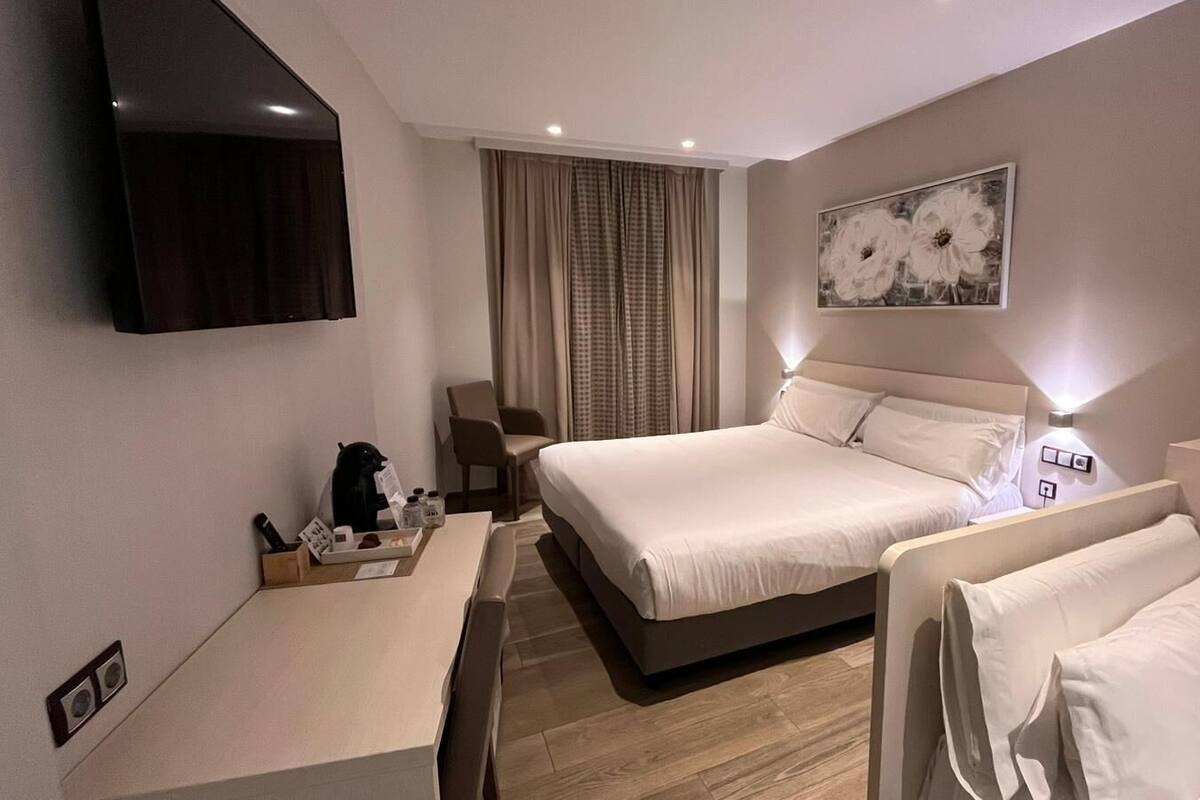 A hotel room with a bed, a desk, a chair, a TV, and a painting on the wall.