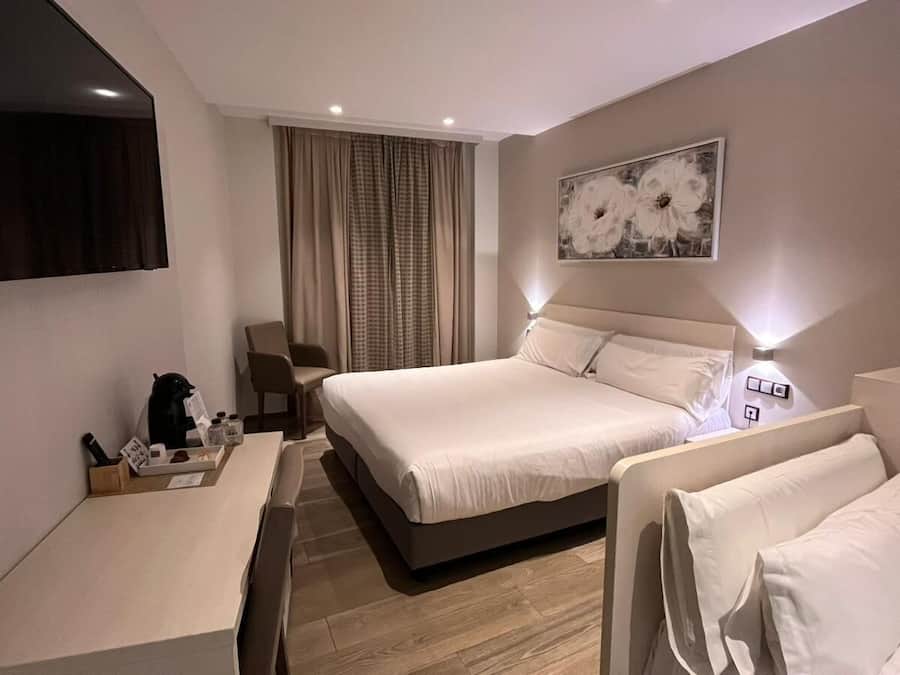 A hotel room with a bed, a desk, a chair, a TV, and a painting on the wall.