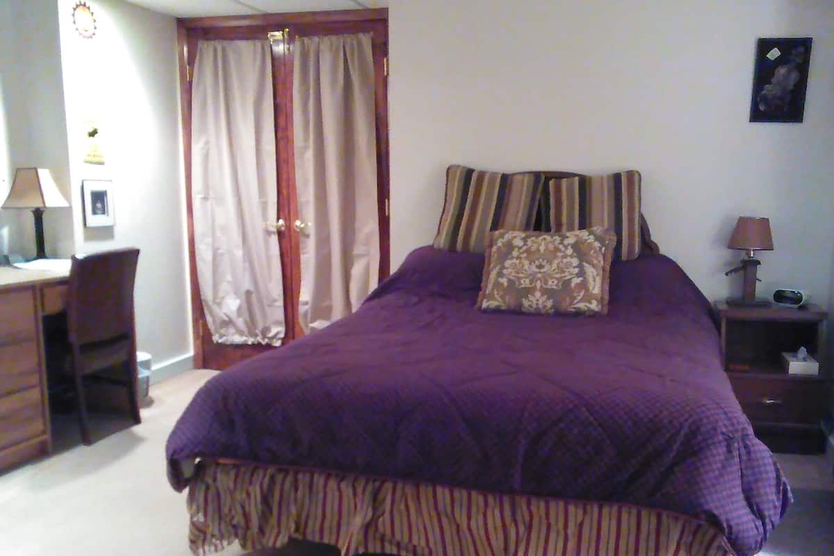 A bedroom with a large bed, a desk, a chair, and a nightstand.