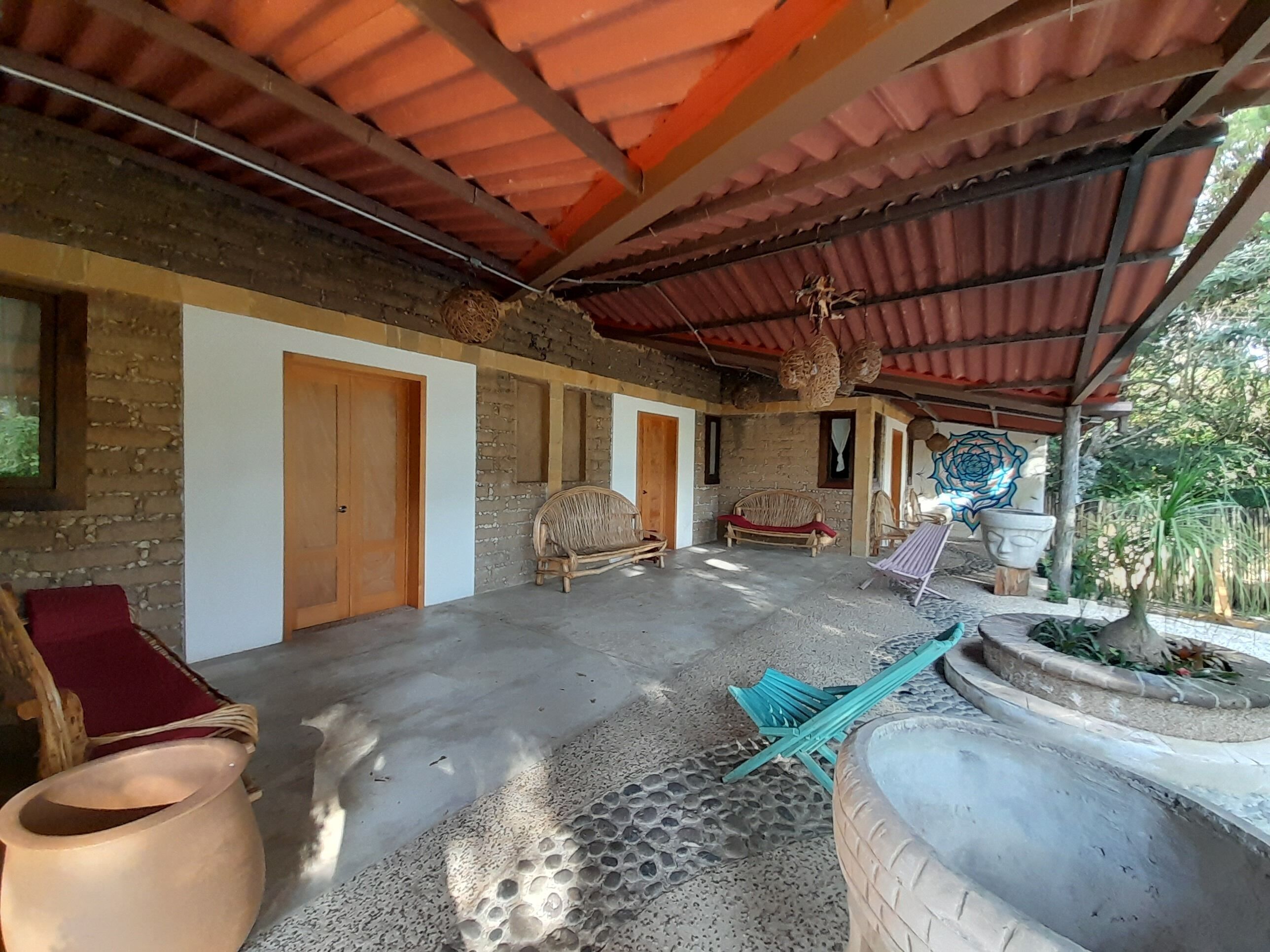Una habitación rústica con piso de baldosas, puertas de madera y una zona cubierta con techo rojo.