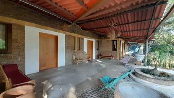 Una habitación rústica con piso de baldosas, puertas de madera y una zona cubierta con techo rojo.