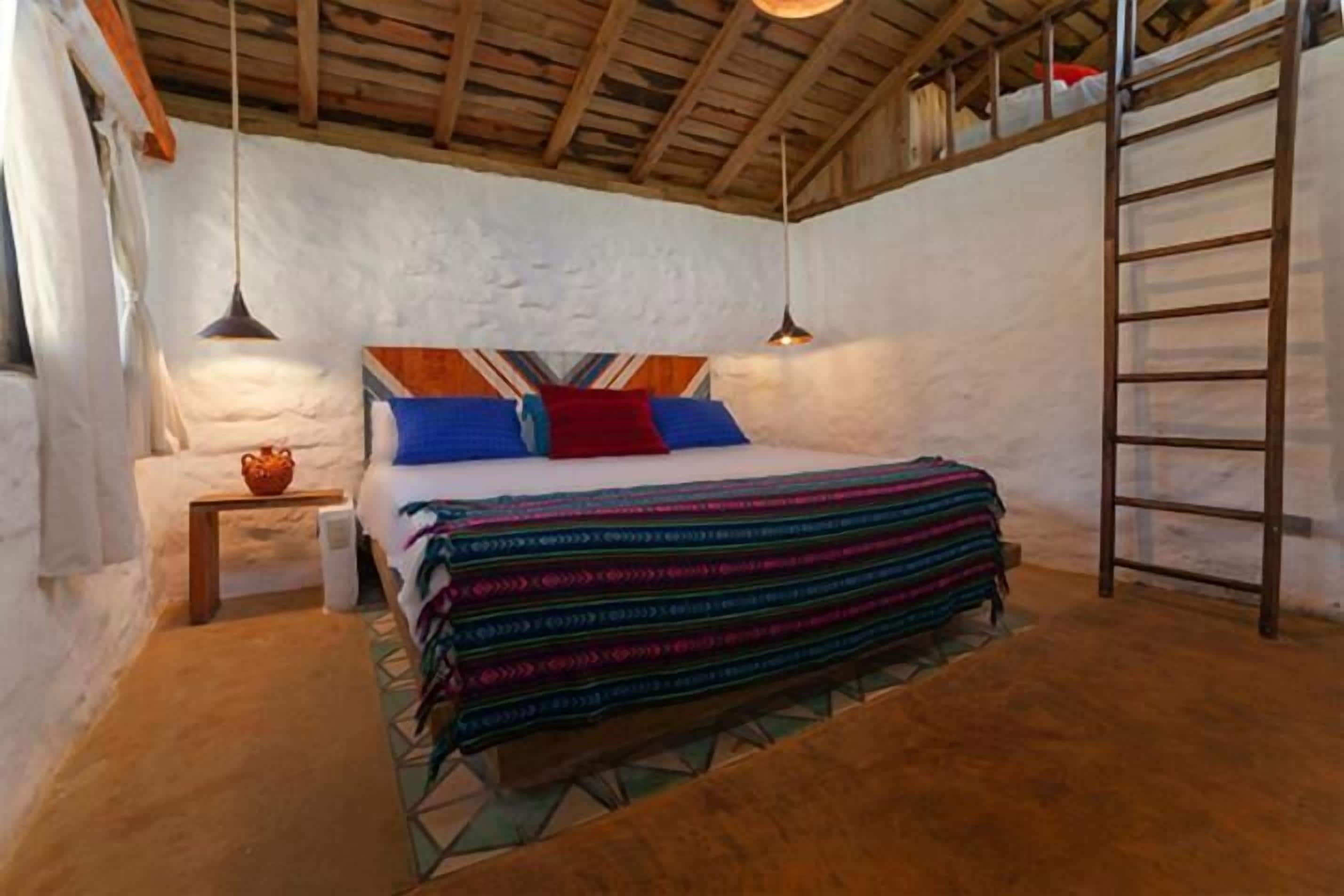 Une chambre confortable avec un lit, des oreillers, une table de chevet, une lampe et une échelle.