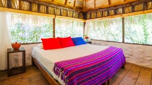 A wooden-framed room with a bed, a nightstand, and a window with a view of greenery. - Canto del Agua Ecolodge (Tzimol)