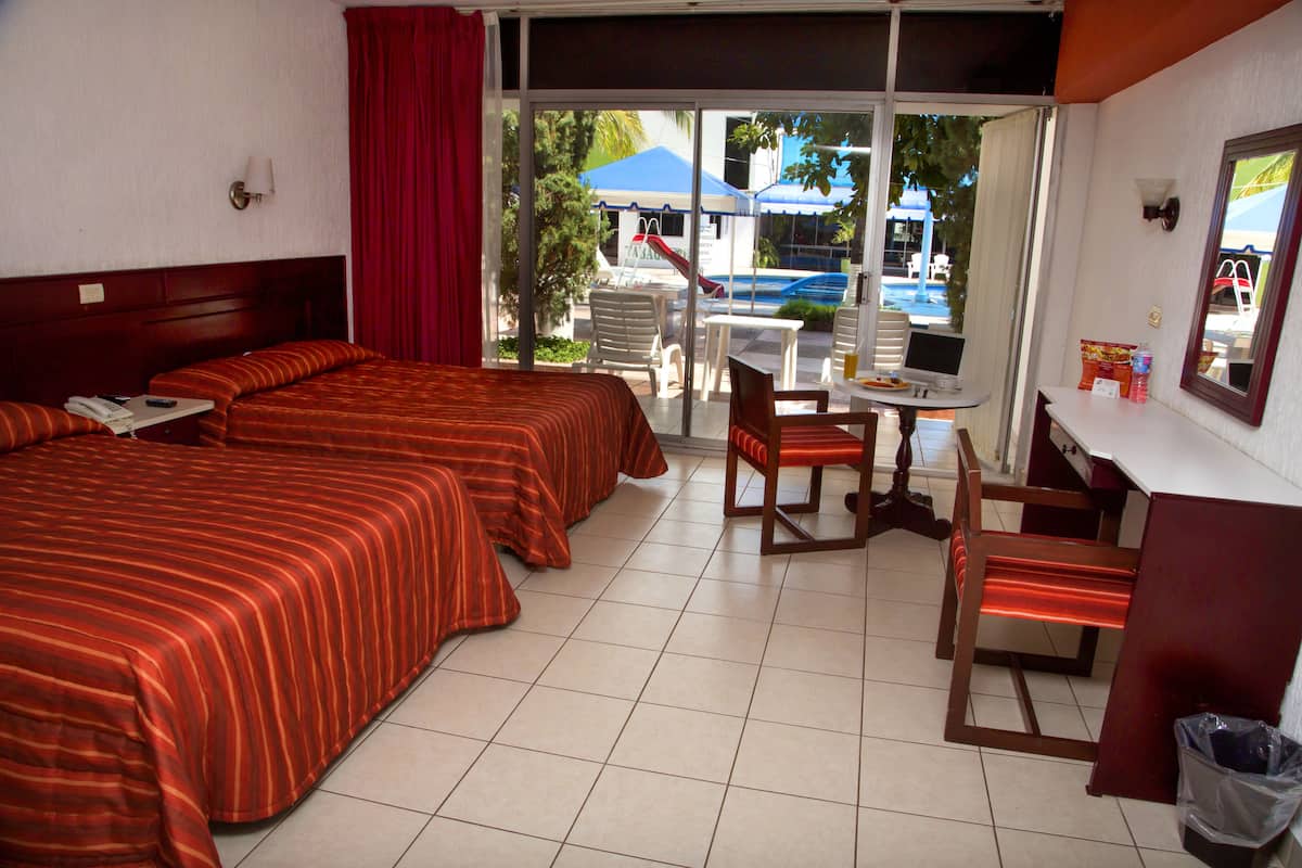 A hotel room with two beds, a desk with a chair, a laptop, and a view of the outside.