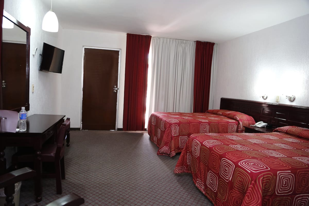 A hotel room with two beds, a desk, a chair, a television, and a door.