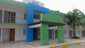 A building with a green and blue facade, a covered entrance, and a palm tree in the courtyard. - Hotel York (Guamuchil)