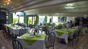 A restaurant with multiple tables, each set with white tablecloths and green table runners, featuring chairs and a tiled floor. - Hotel York (Guamuchil)