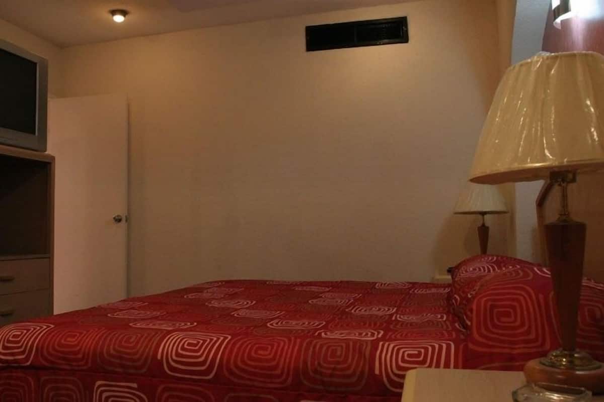 A bedroom with a bed, a dresser, a television on top, a lamp, and a window.