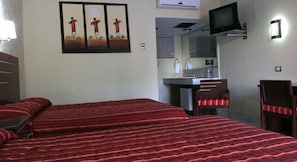 Quarto de hotel com uma cama, uma escrivaninha, uma cadeira, uma televisão e um espelho.