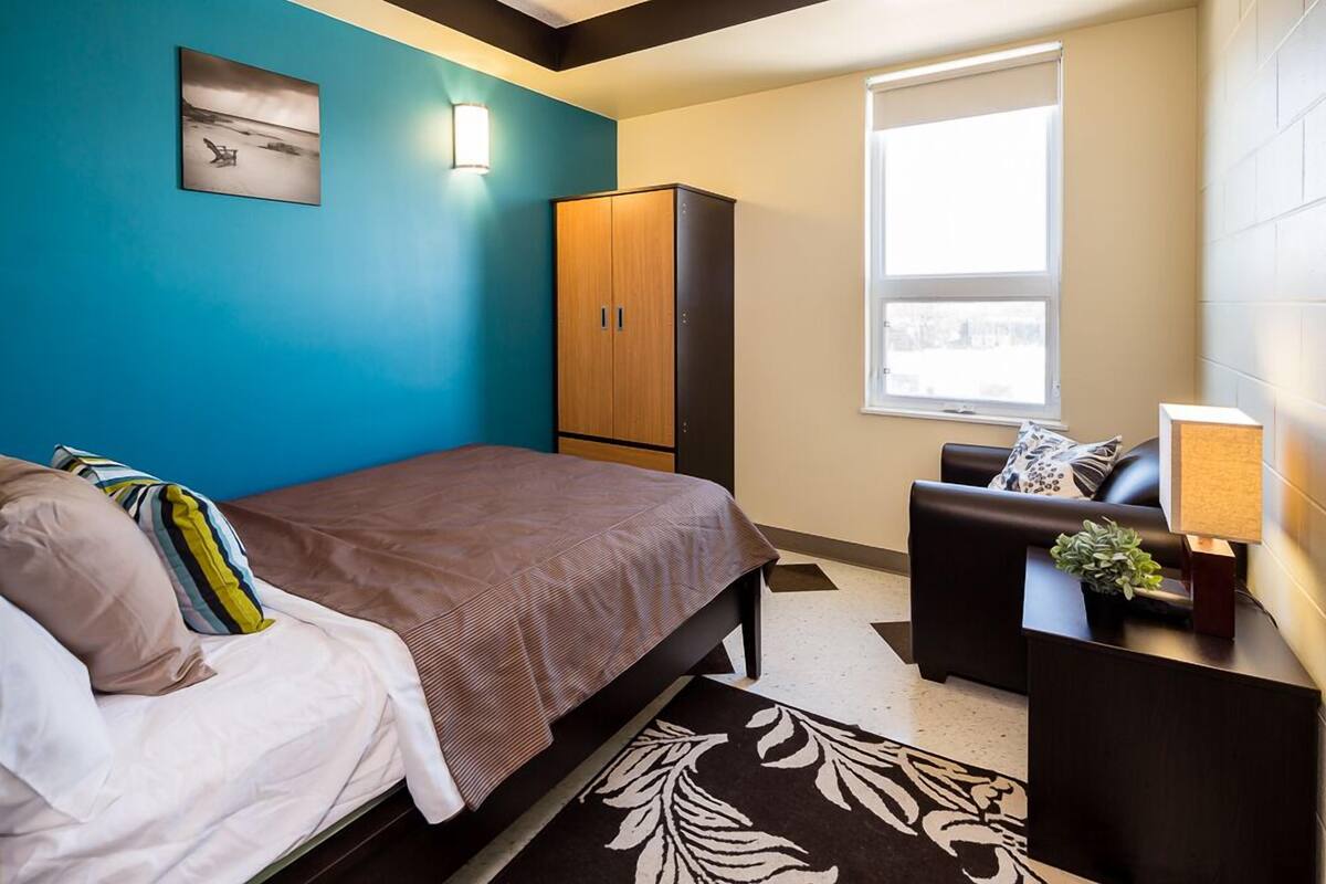 A bedroom with a bed, a wardrobe, a desk with a lamp, and a window.