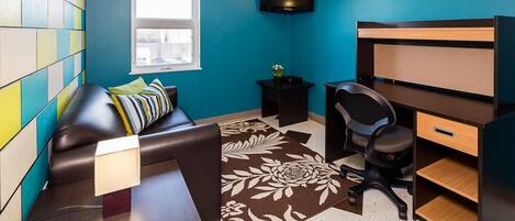 Une pièce moderne avec un mur d’accent de couleur turquoise, un canapé en cuir noir, un bureau en bois, un fauteuil de bureau noir et un grand tapis à motifs floraux.