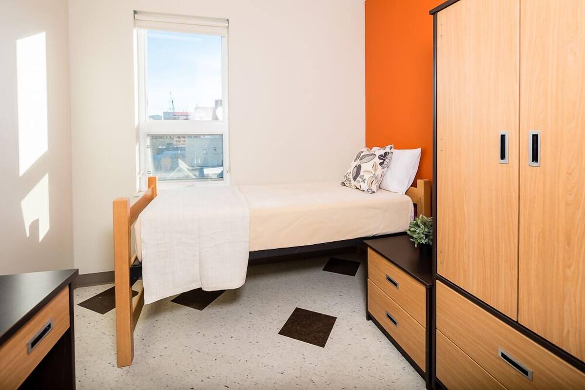 A small, neatly arranged bedroom with a bed, a window, a wardrobe, and a desk.