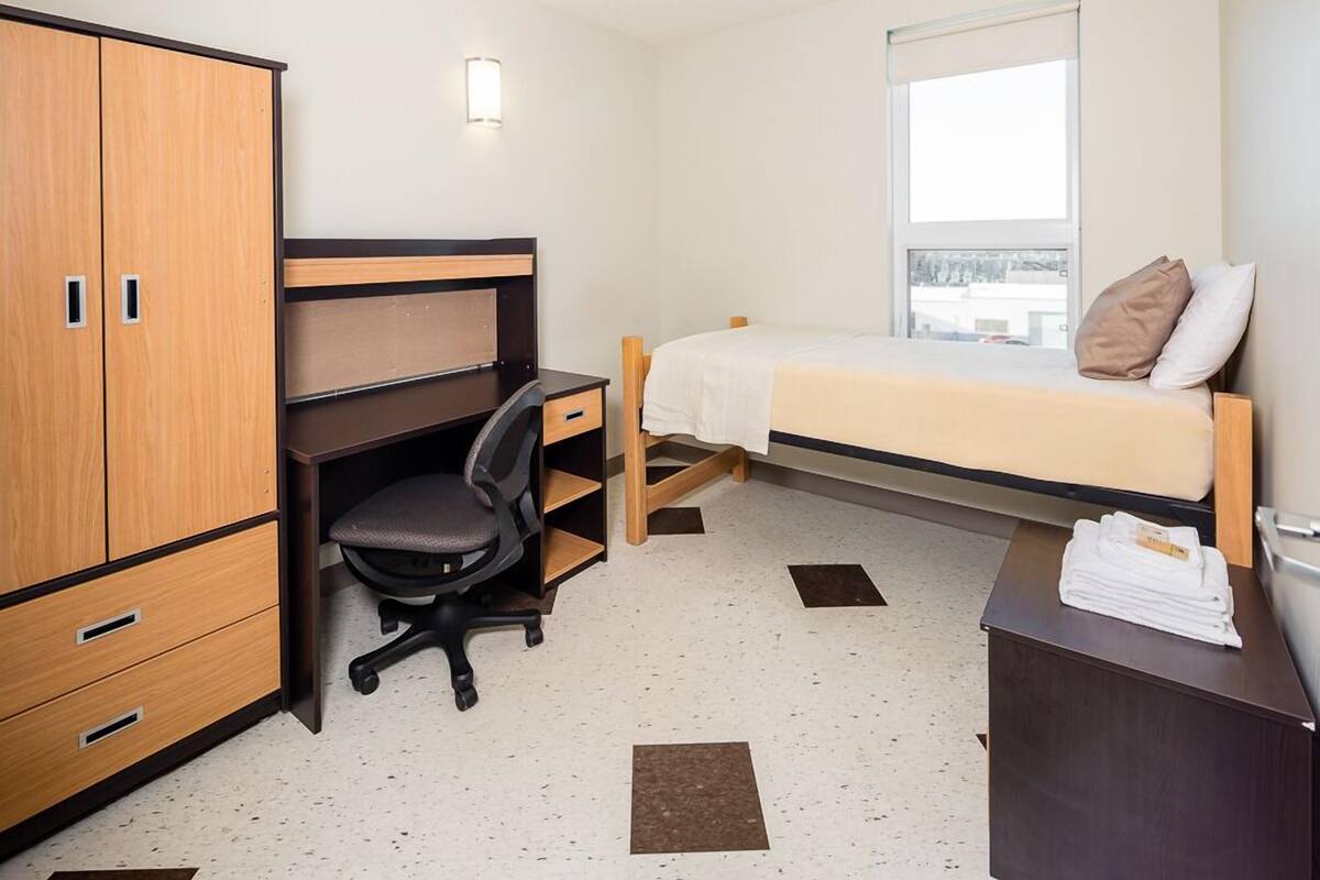 A compact room with a bed, a desk with a chair, a wardrobe, and a window.