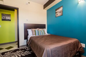 Une chambre d’hôtel avec un lit, une tête de lit, un mur orné d’un tableau et une porte.