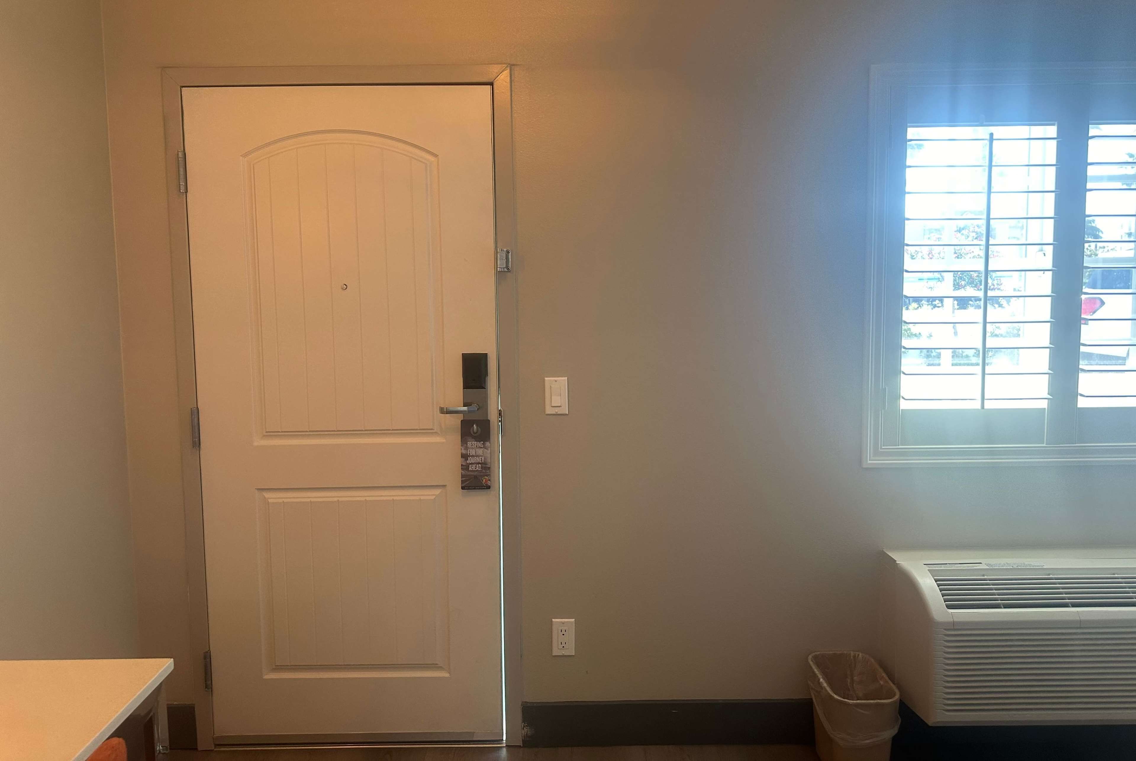A room with a white door, a window with blinds, and a wall-mounted air conditioner.