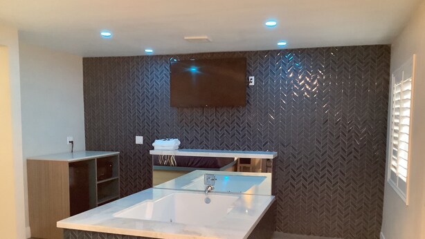 A modern bathroom with a large central sink, a mirror above it, and a herringbone-patterned wall. - Super 8 by Wyndham Oceanside Downtown (Oceanside)