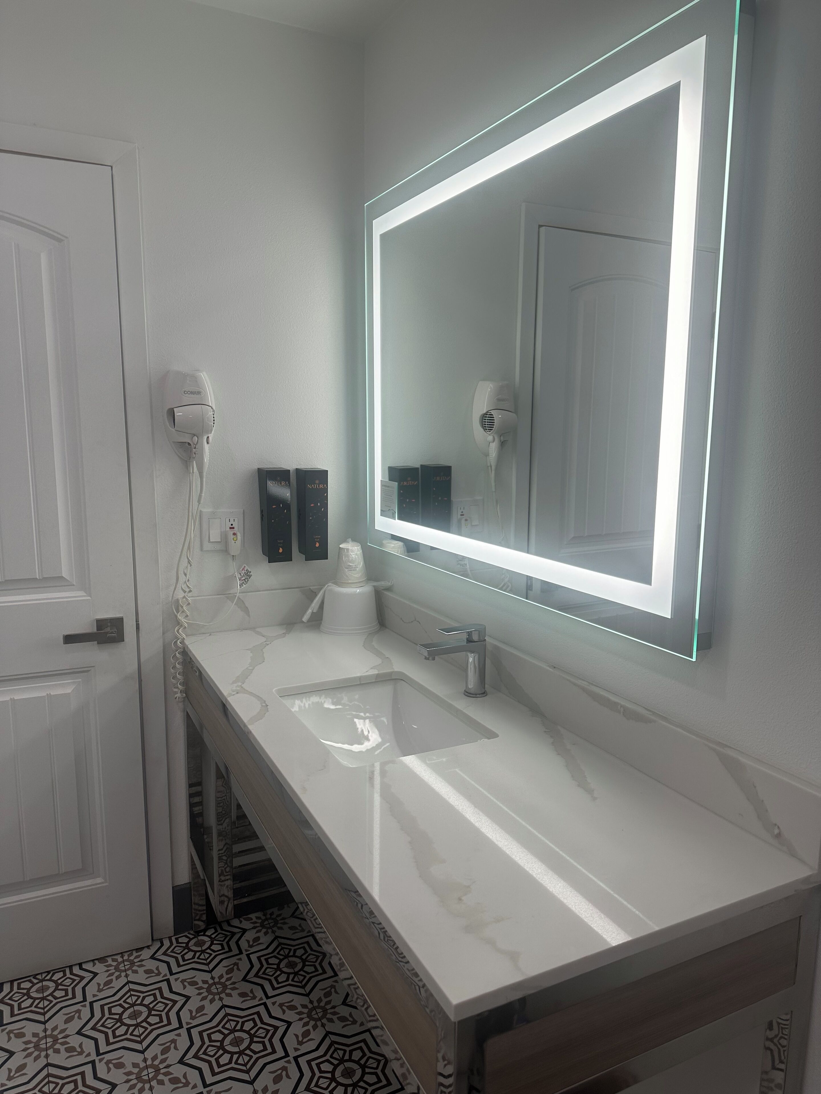 A bathroom with a large mirror, a sink, and a hairdryer.