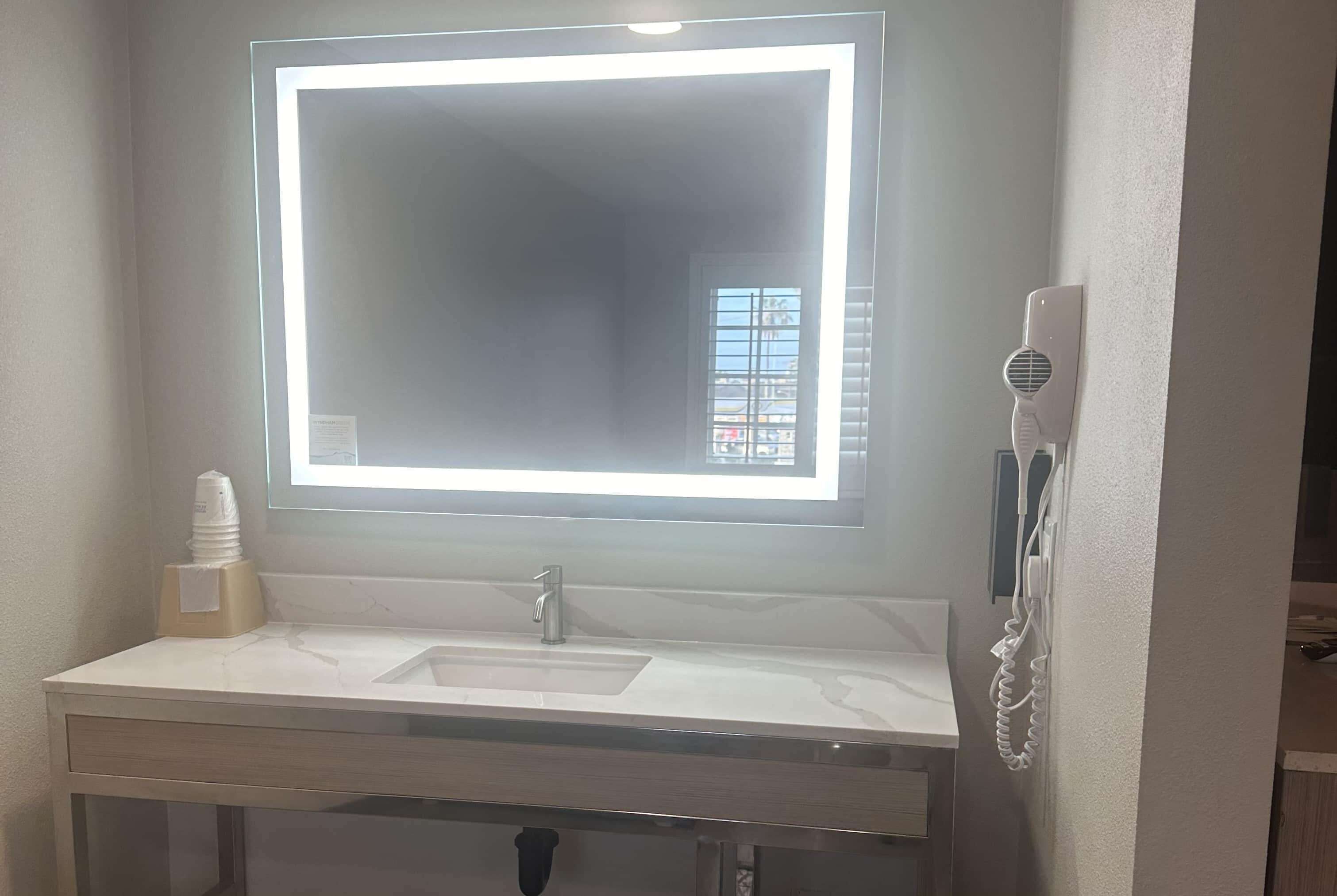 A bathroom with a large mirror, a sink, a towel dispenser, and a hairdryer.