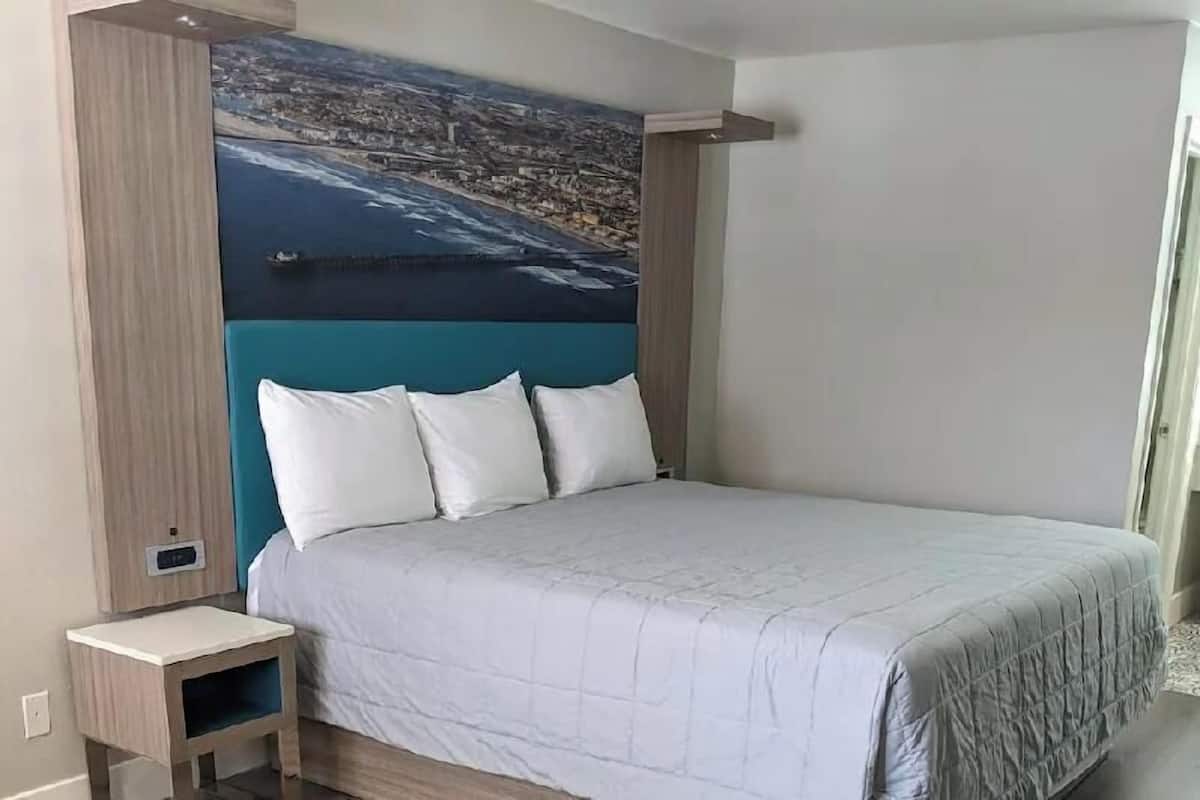 A bedroom with a bed, a nightstand, a wall-mounted shelf, and a cityscape painting.