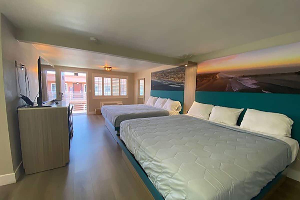A hotel room with two beds, a desk, and a large painting of a sunset over the ocean.