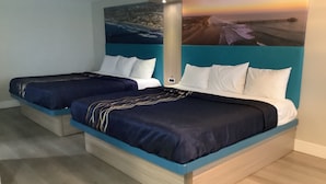 A hotel room with two single beds, each with a blue headboard and white bedding. The room has a wooden floor and a large painting of a coastal scene on the wall. - Super 8 by Wyndham Oceanside Downtown (Oceanside)