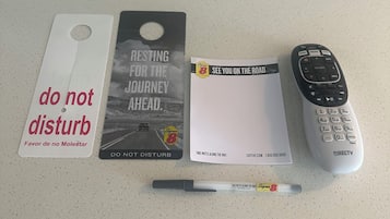 A table with a 'Thank You For Not Smoking' sign, a 'Do Not Disturb' sign, a 'Resting for the Journey Ahead' card, a 'See You on the Road' card, a DIRECTV remote control, and a pen.