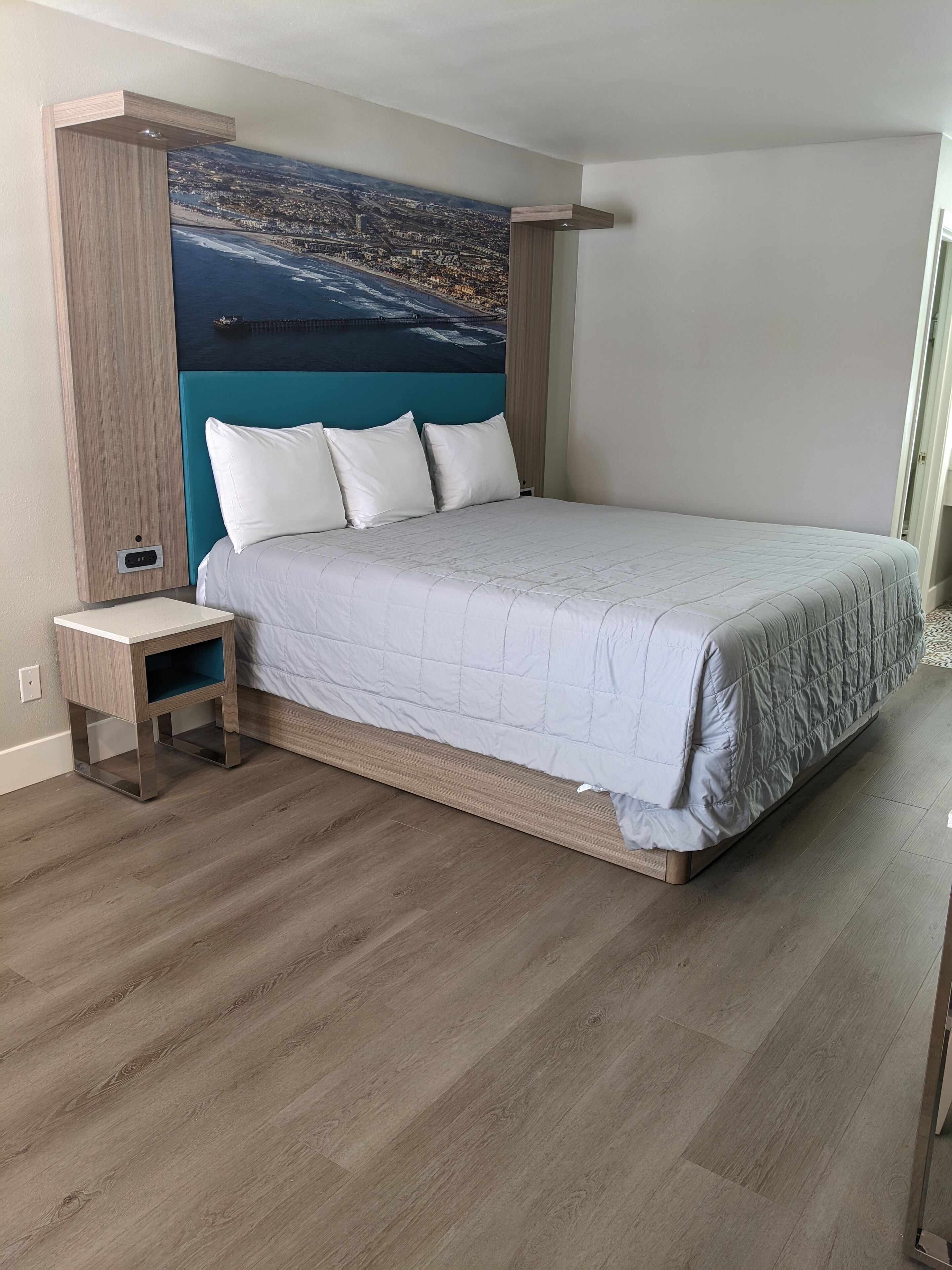 A modern bedroom with a large bed, a nightstand, and a cityscape mural on the wall.