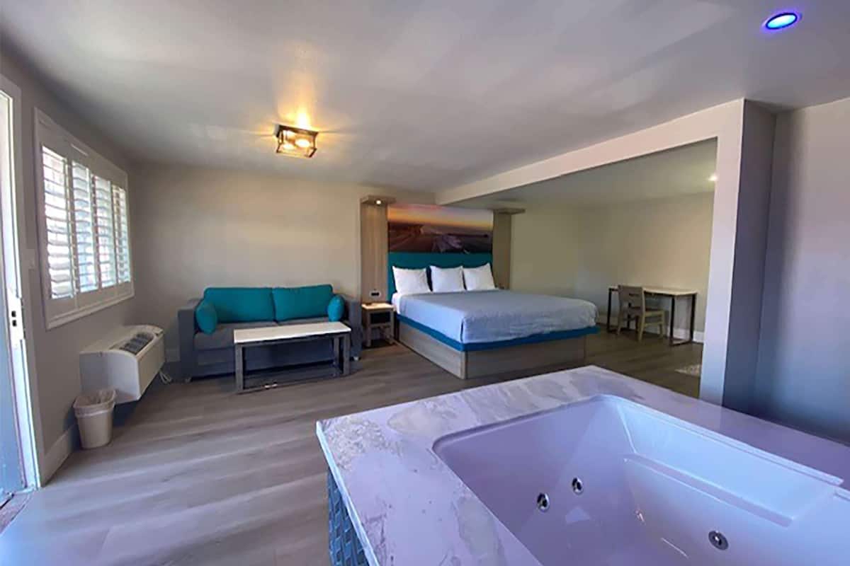 A modern bedroom with a large bed, a sofa, a small table, and a bathtub.