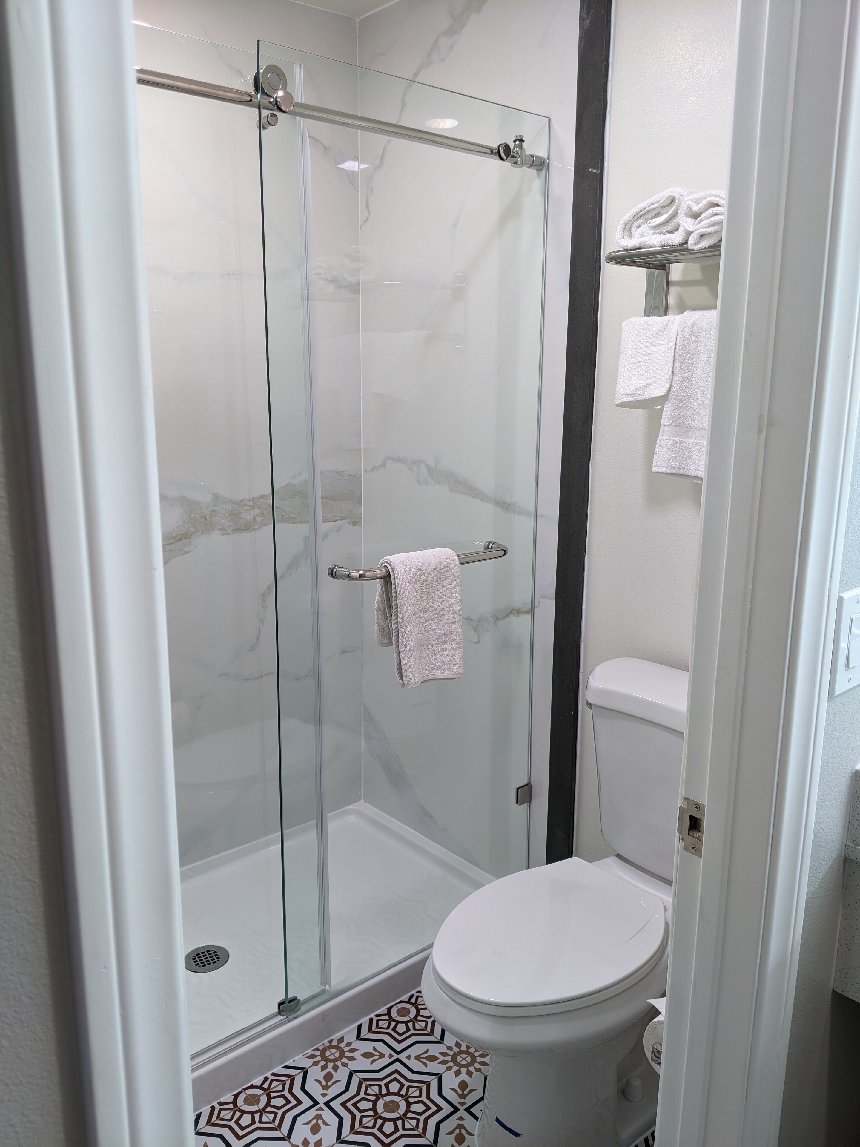 A glass-enclosed shower stall with a towel rack and a toilet with a patterned floor.