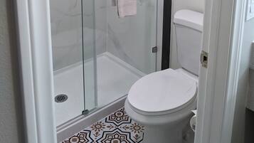 A glass-enclosed shower stall with a towel rack and a toilet with a patterned floor.