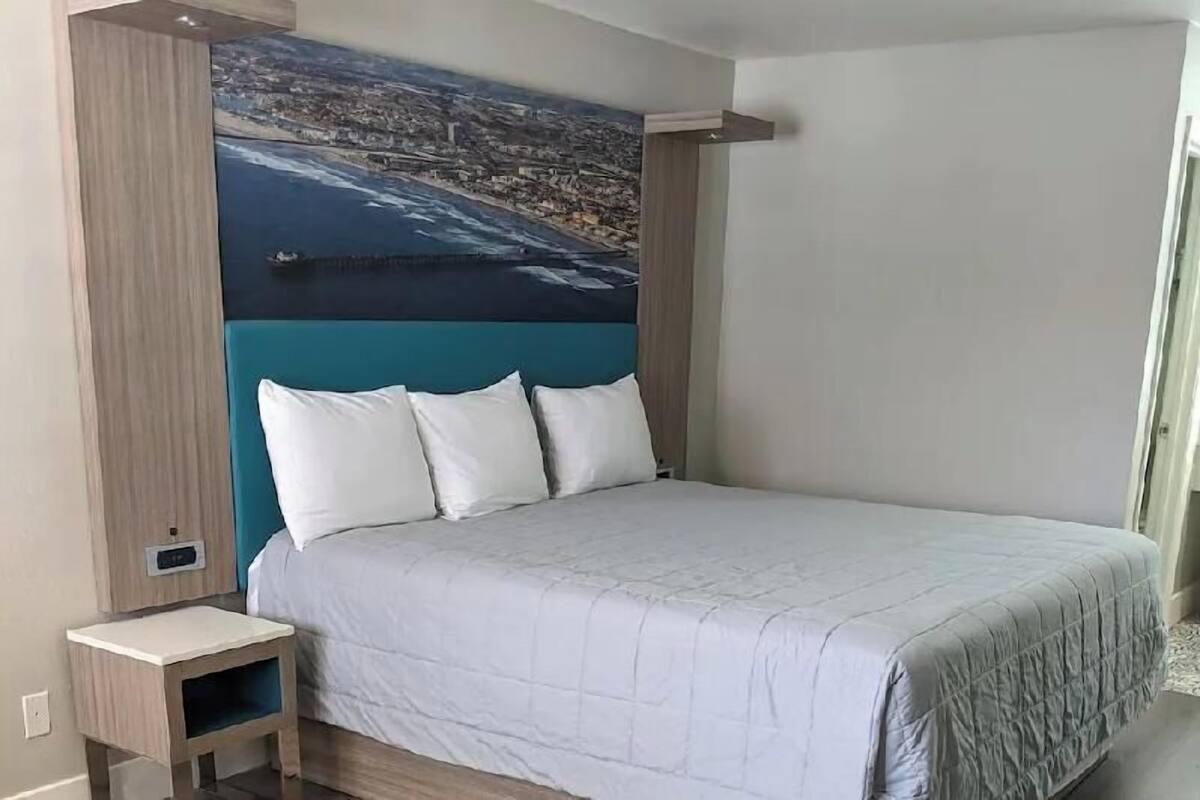 A bedroom with a bed, a nightstand, a wall-mounted shelf, and a cityscape painting.