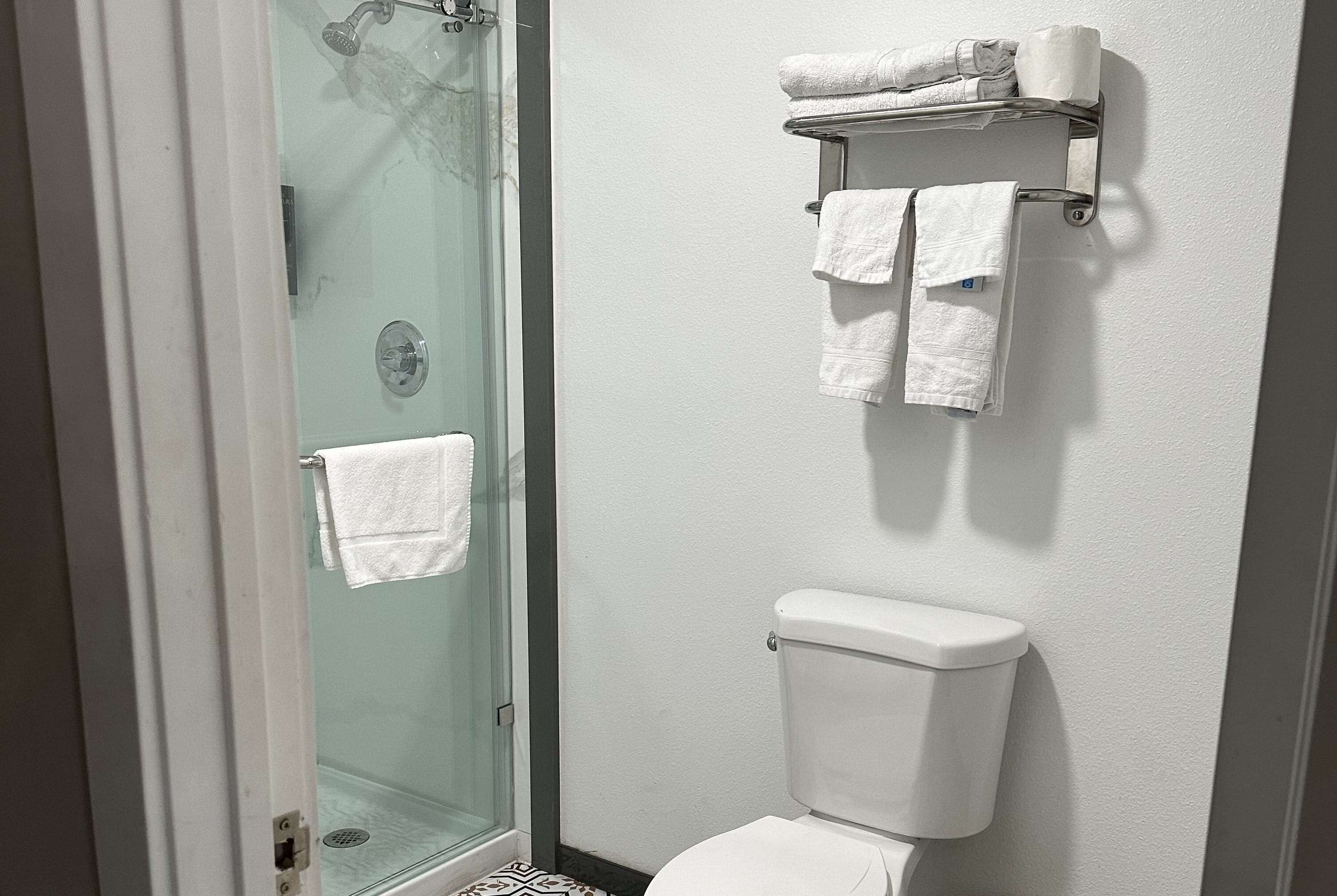 Un baño con cabina de ducha de vidrio, inodoro y toallero con toallas dobladas.
