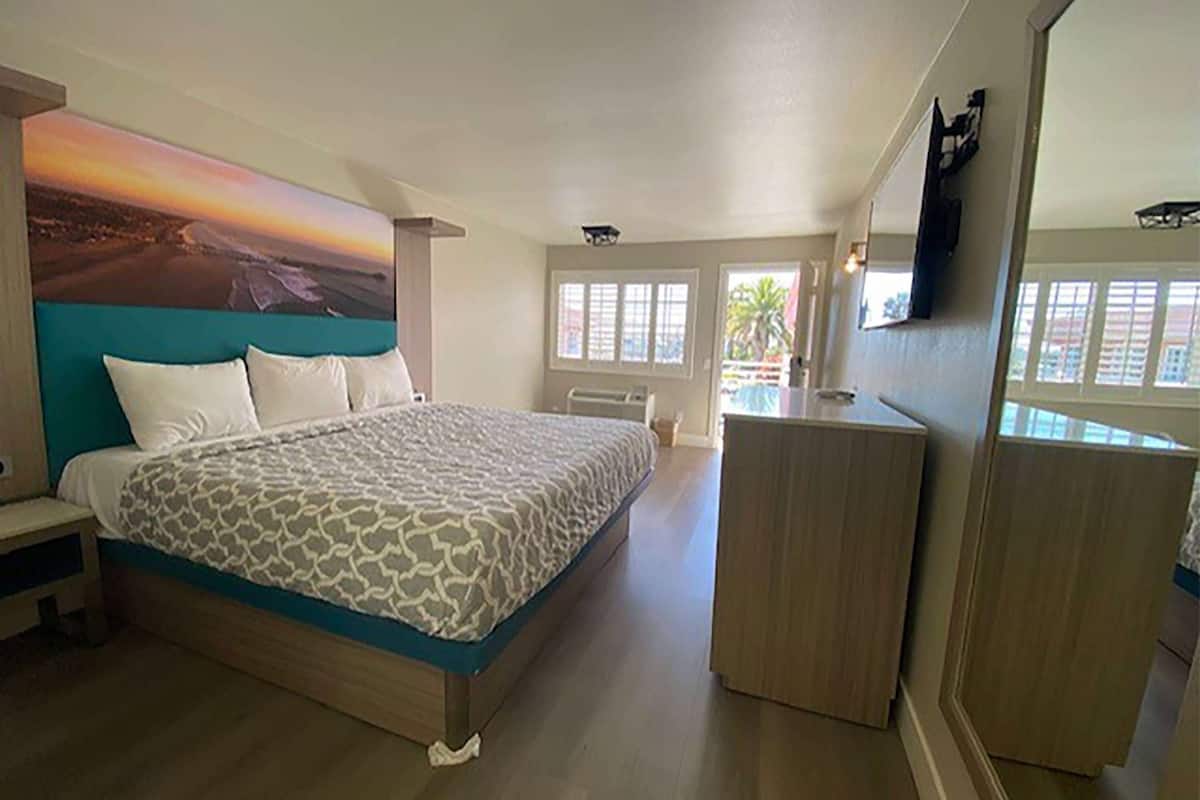 A bedroom with a bed, a desk, and a large window.